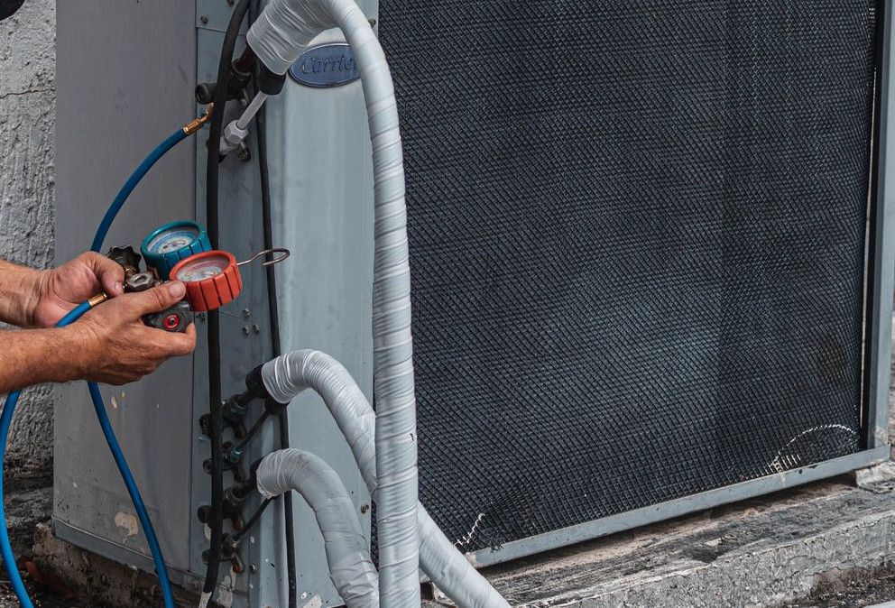 Technician repairing an air conditioner unit outdoors, wearing a facemask and using a manifold gauge.