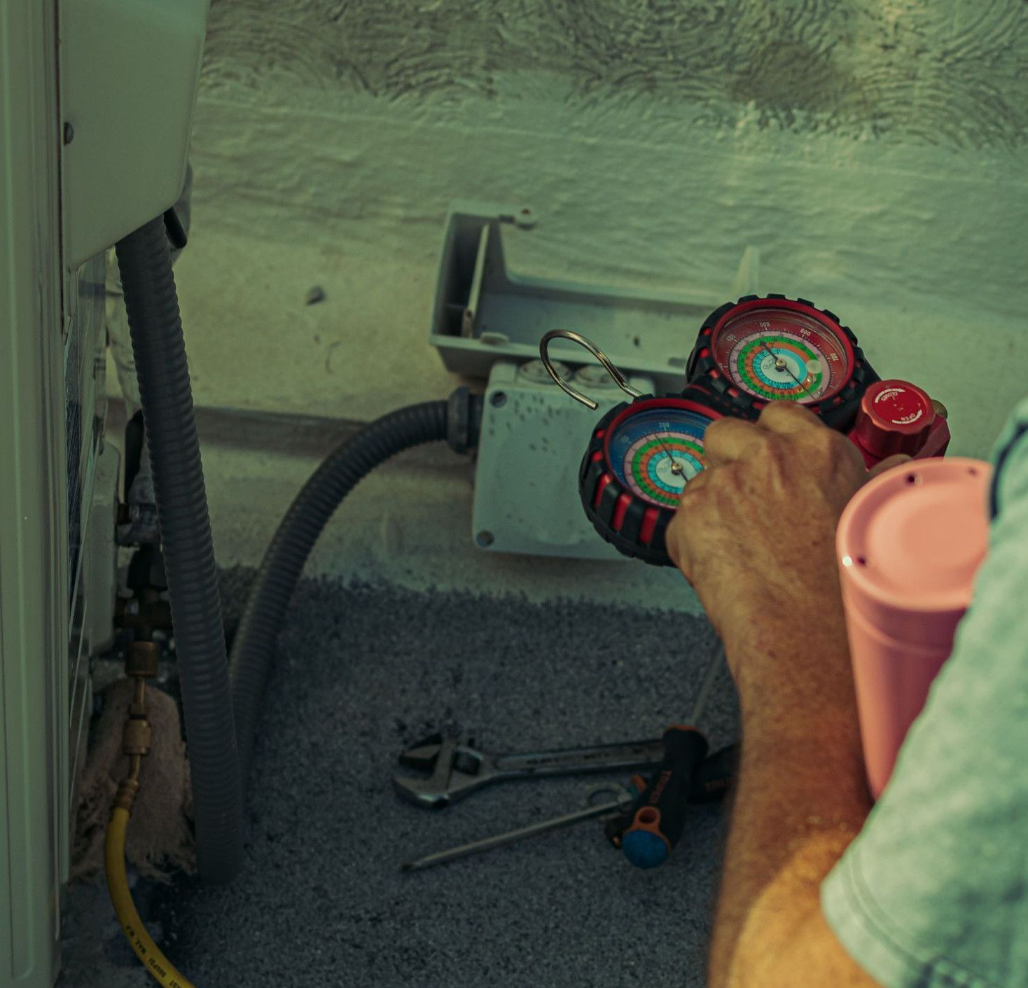 A technician checks and repairs an HVAC system outdoors using tools and gauges.
