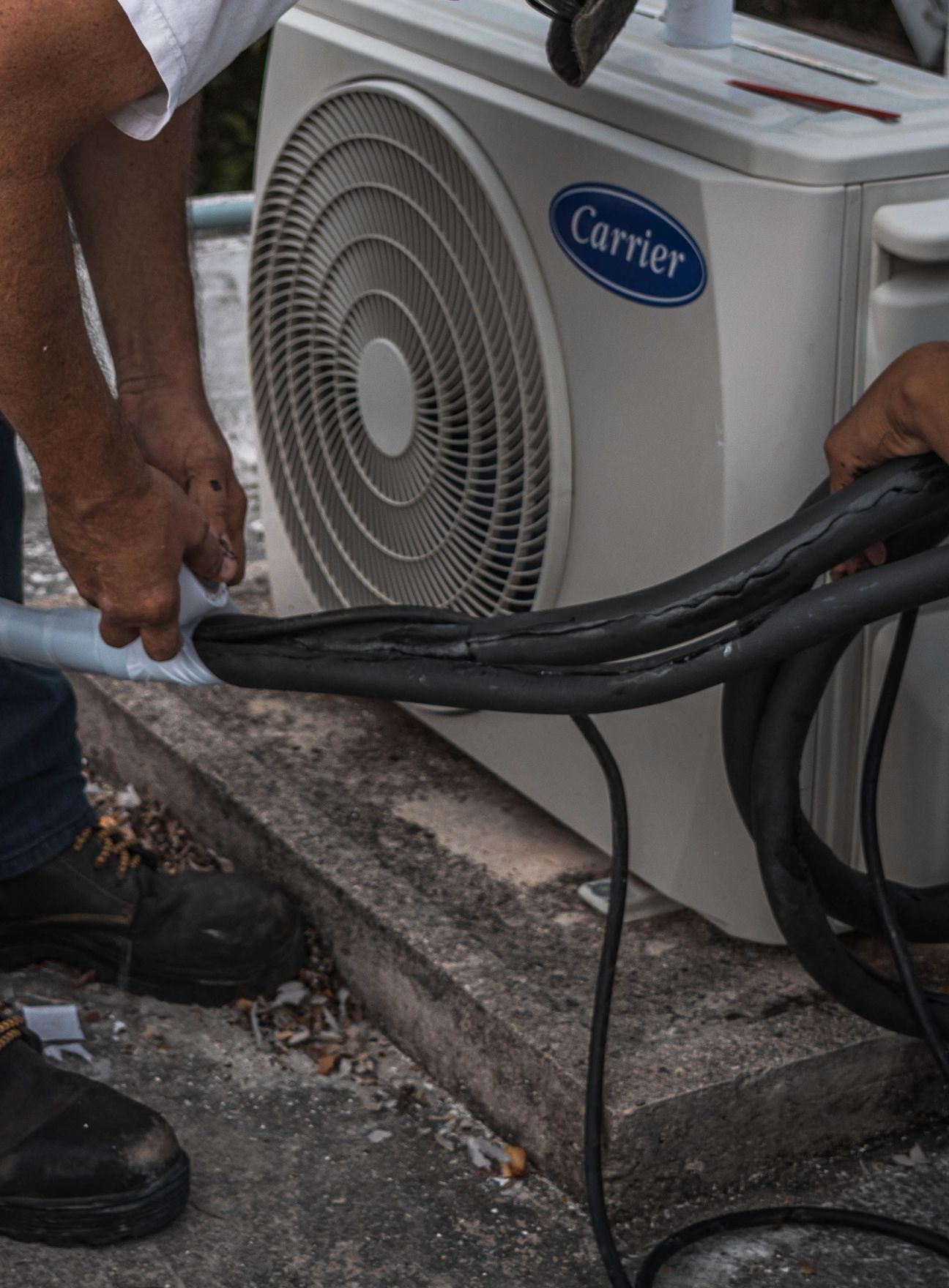A technician performs maintenance on an outdoor air conditioning unit, focusing on hose connections.